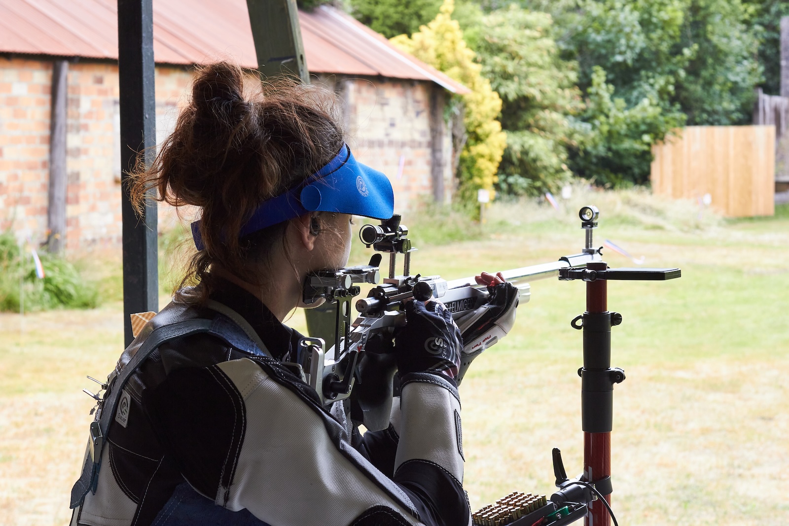 A female target shooter aims her rifle from the kneeling position on an outdoor shooting range. She wears a heavy black and white jacket to steady her aim. Credit: Richard Hemingway