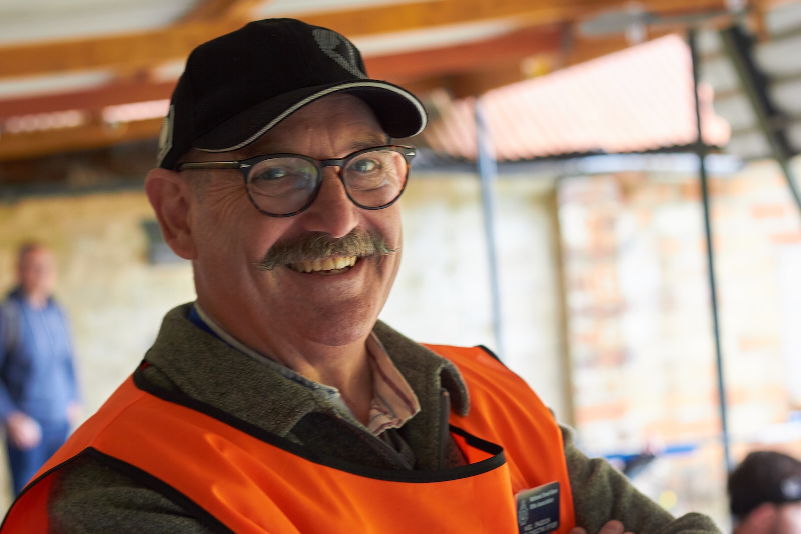 A smiling man with a moustache and wearing a high viz jacket stands on a shooting range supervising a competition. Credit: Richard Hemingway
