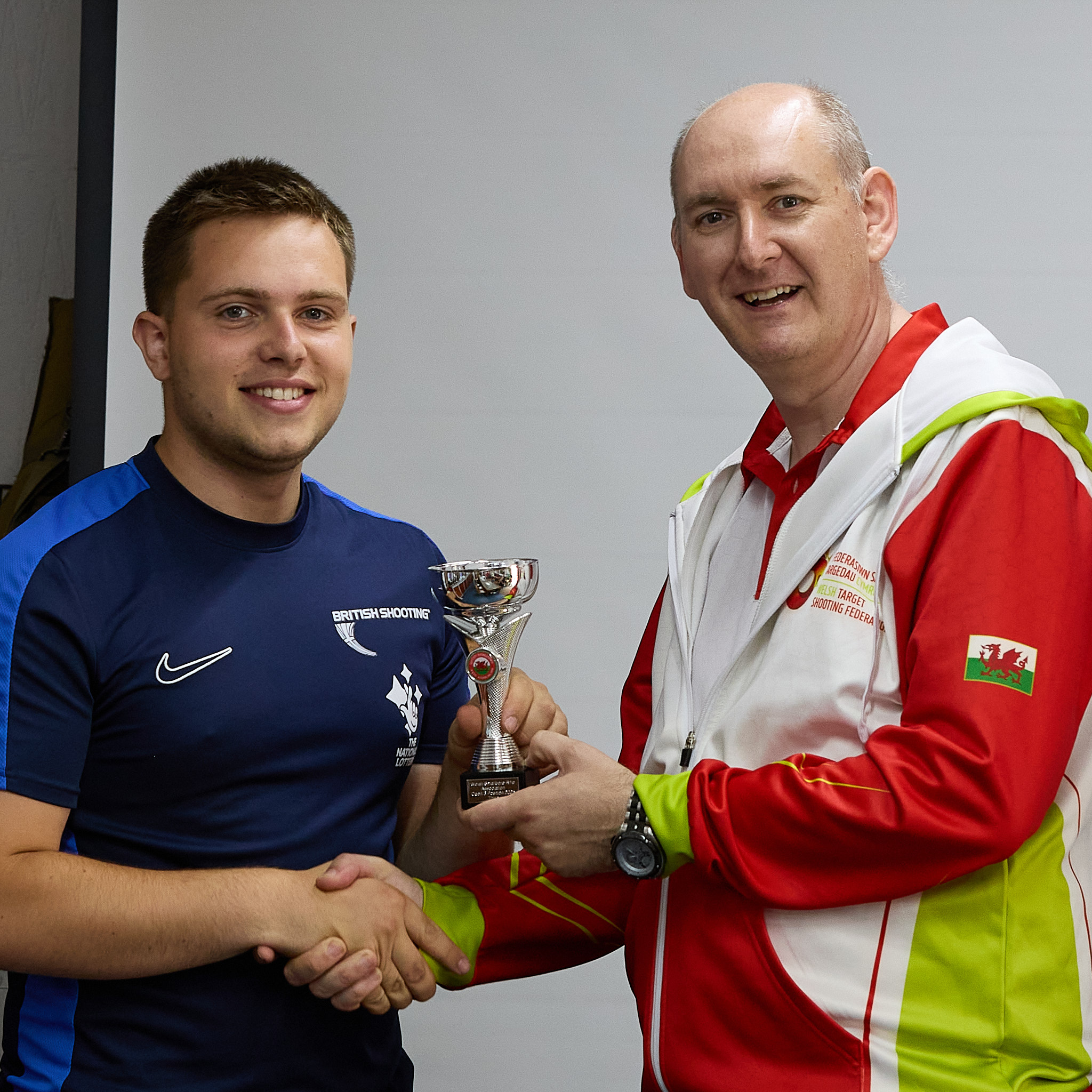 Two people stand in front of a projection screen. The man in a red, white and green top presents a prize to an athlete.