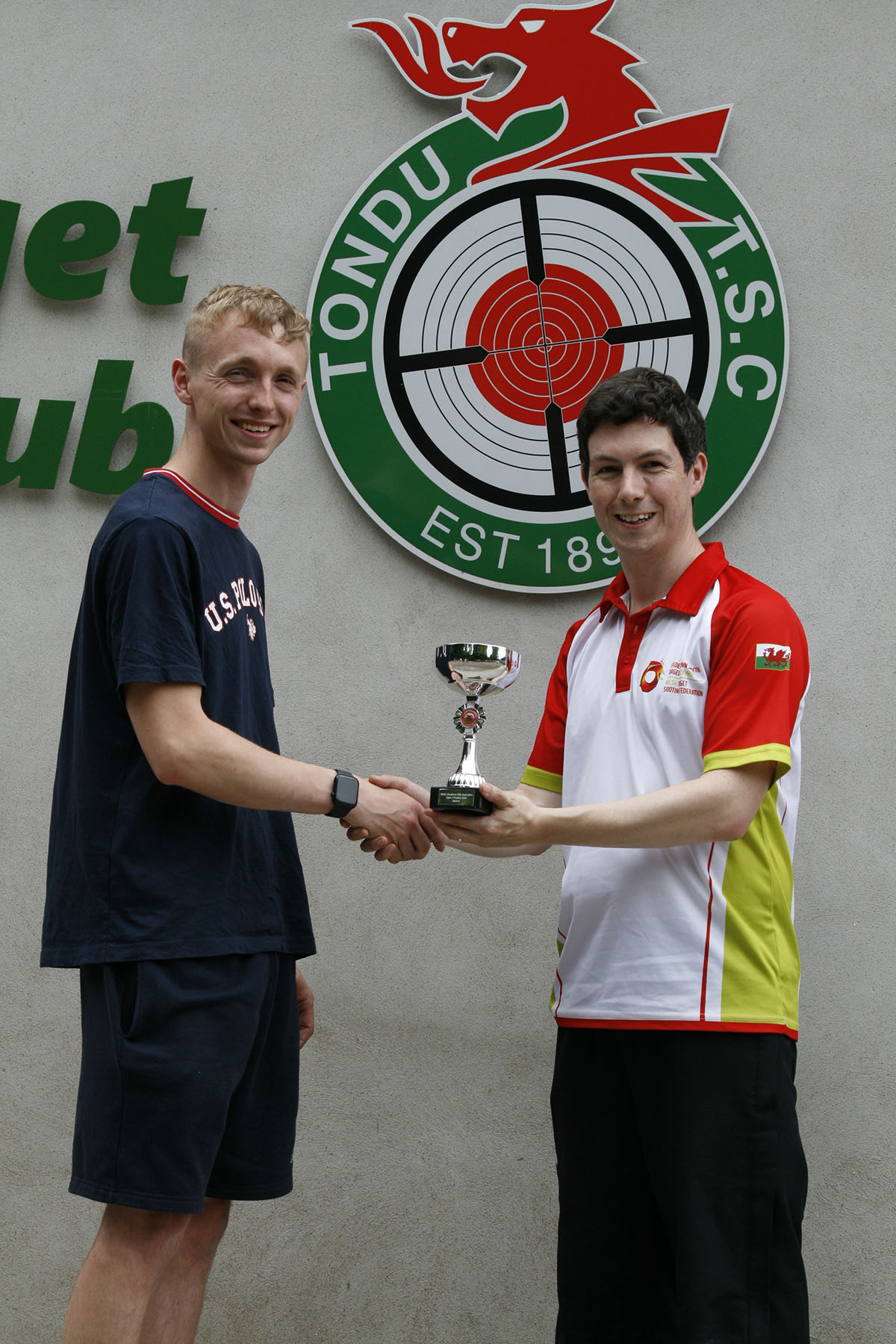 A man in a red and white top presents a trophy to an athlete in t-shirt and shorts. Credit: Niall Evans